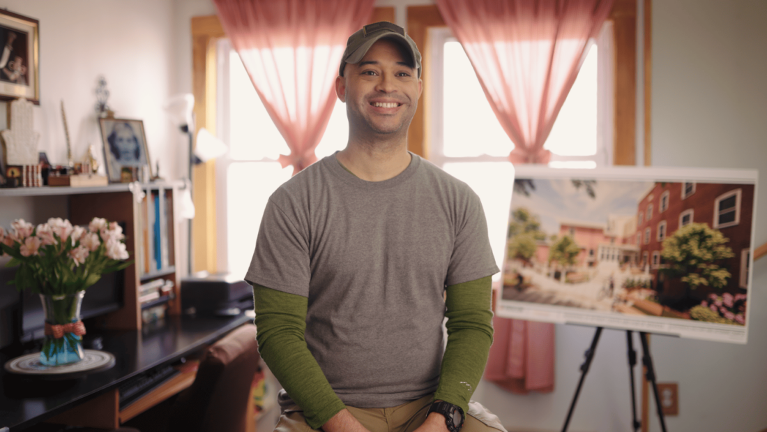 Veterans Count client sitting in char with a map of the Military & Veterans Campus in the background