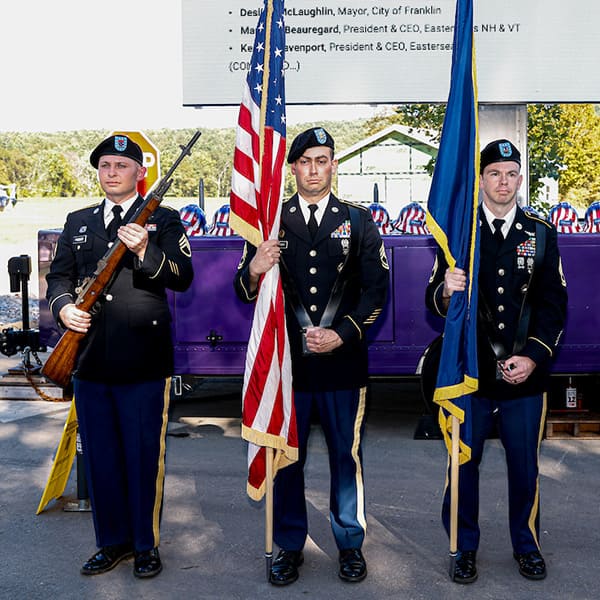 3 US army soldiers in dress uniform standing at attention holding flags and rifle